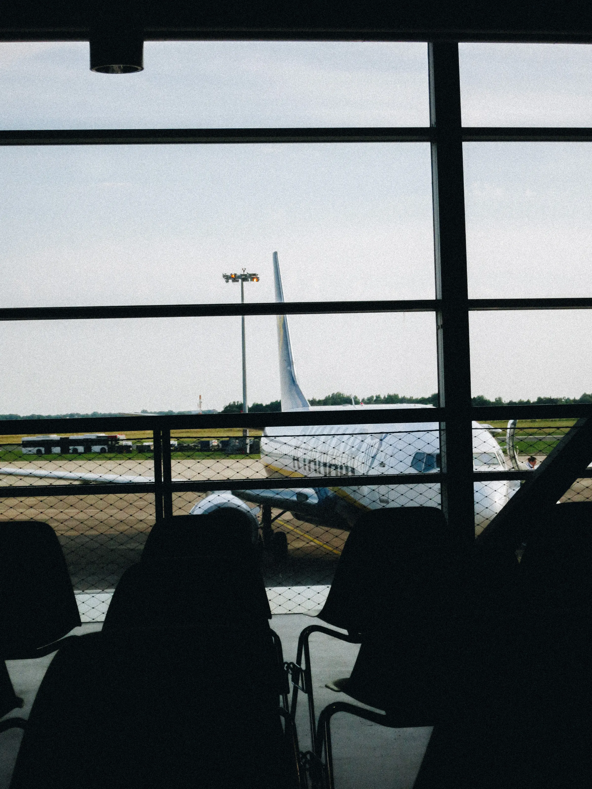 A parked airplane seen through an airport gate window, rows of empty seats in the foreground