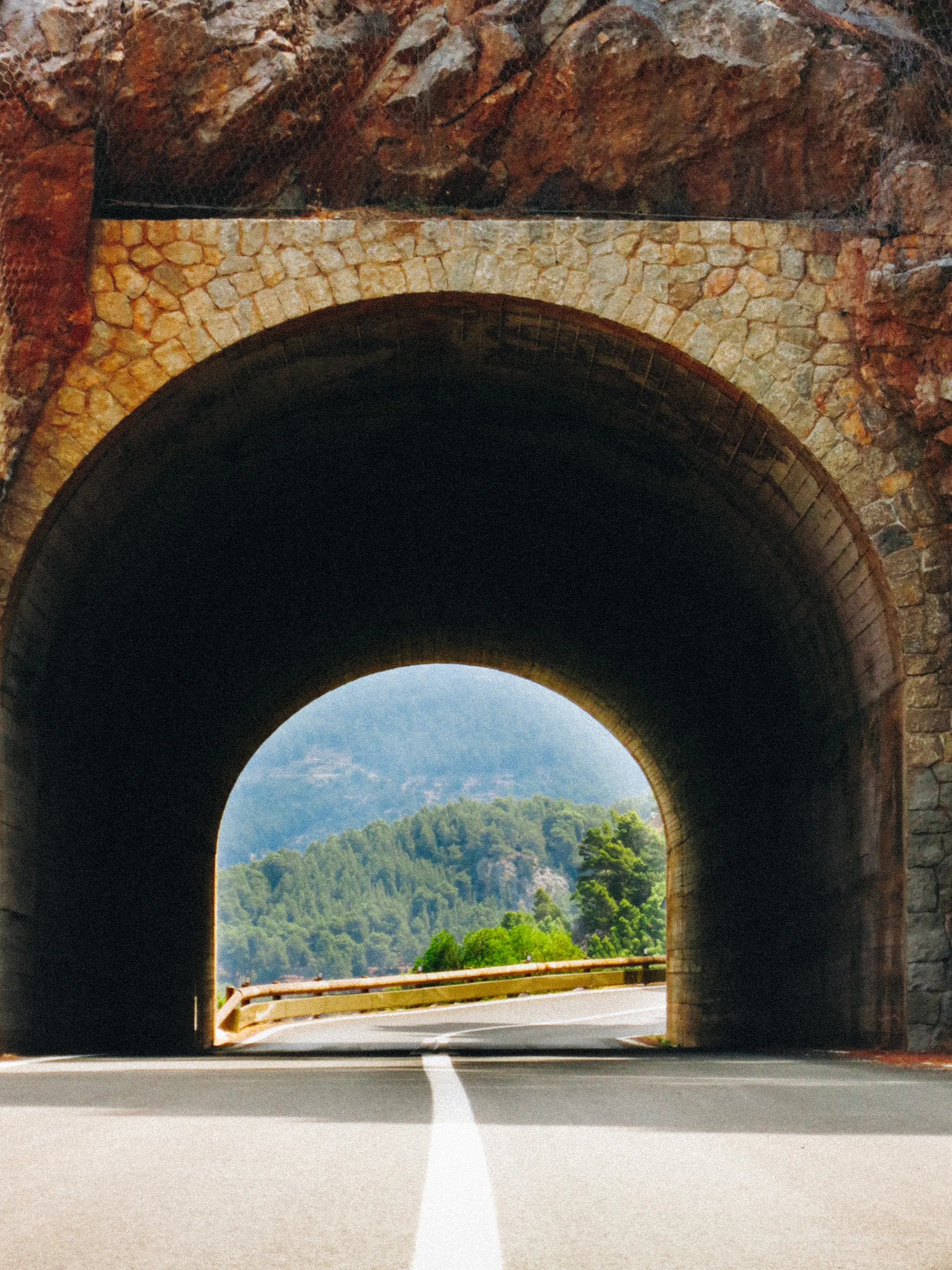 A stone road tunnel with green hills visible through the far opening
