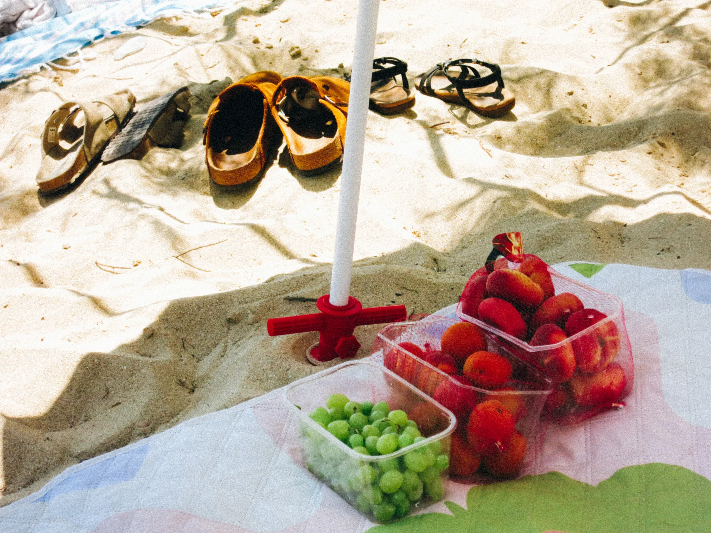 Sandals lined up on the beach next to containers of grapes and apricots