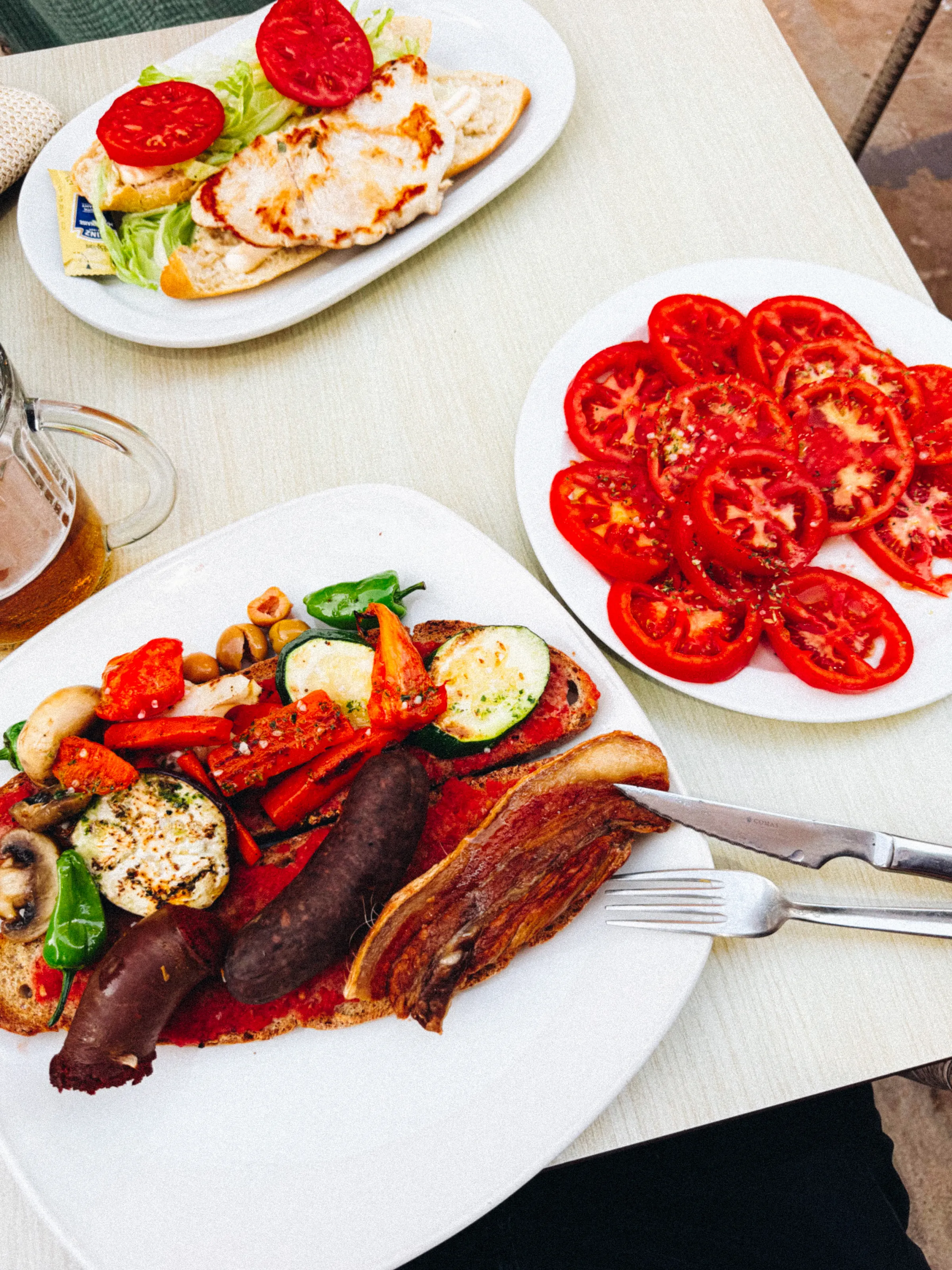 Two plates of food: a grilled chicken baguette with tomato and lettuce, and a plate of sliced tomatoes