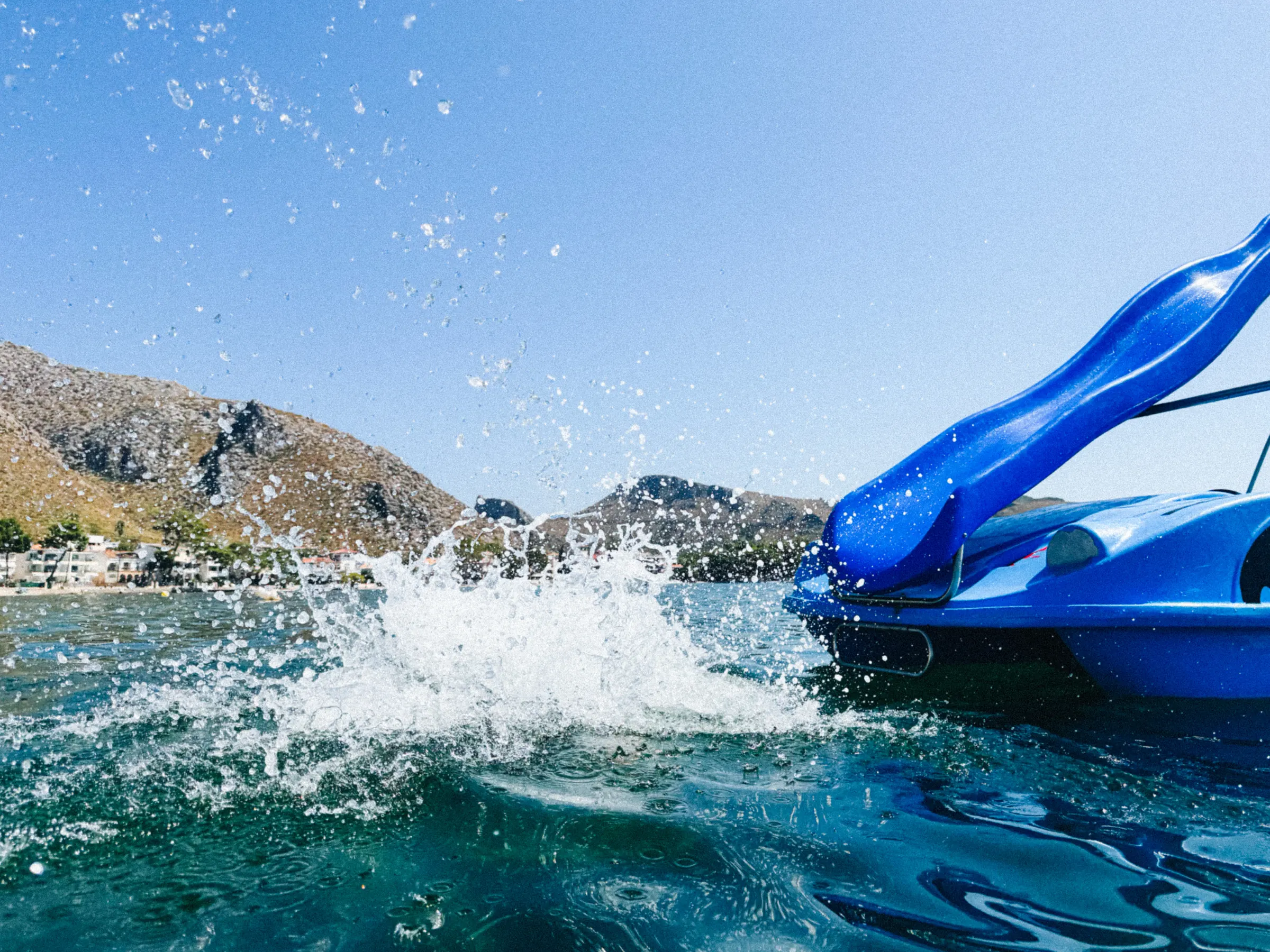 A pedal boat splashing through the water, hills and a coastal town in the background