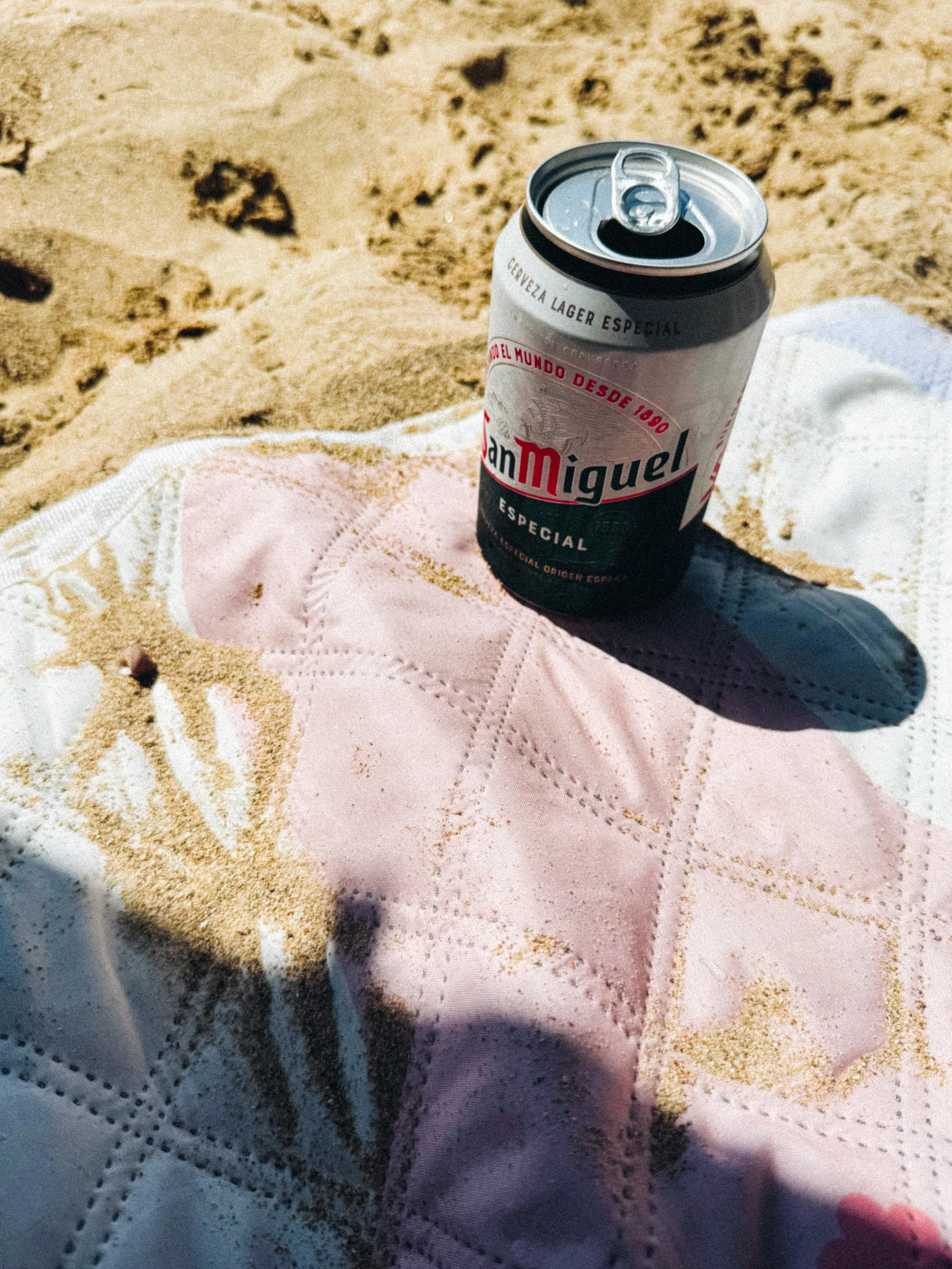 A can of San Miguel beer standing on a sandy beach towel