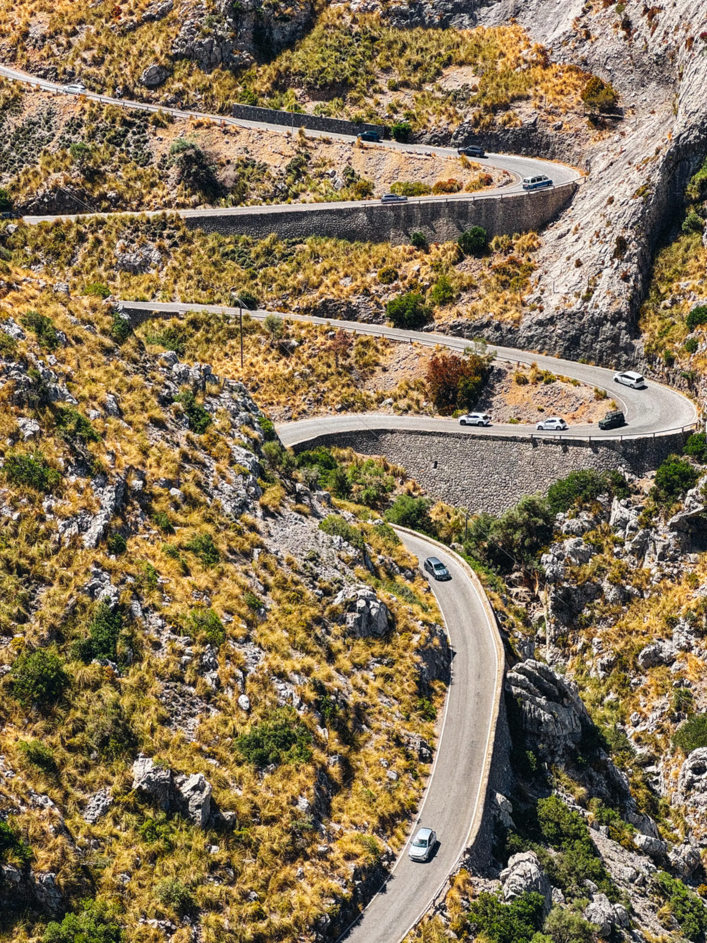 An elevated view of a switchback mountain road with several cars navigating the hairpin turns