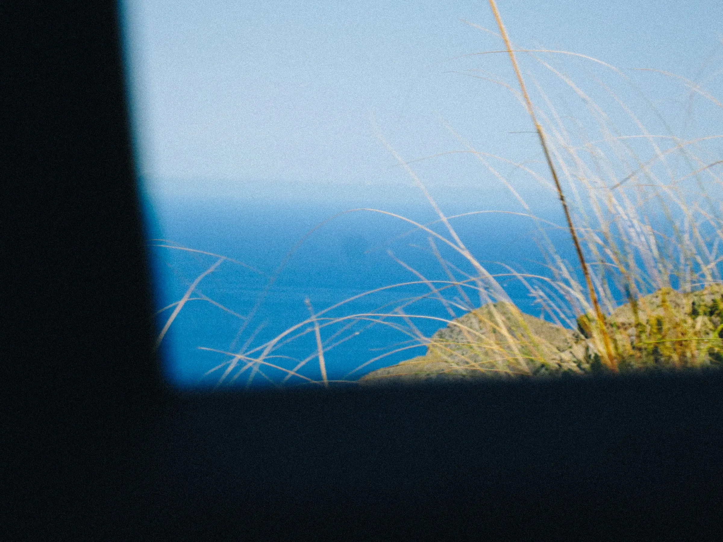 A view of the sea horizon through a car window, dry grass in the foreground